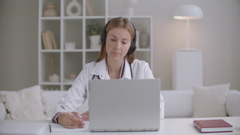 Cita-En-Línea-Con-La-Doctora-Terapeuta-Le-Pregunta-Al-Paciente-Por-Videollamada-En-Una-Computadora-Portátil-Y-Escribe-Notas-En-Un-Cuaderno